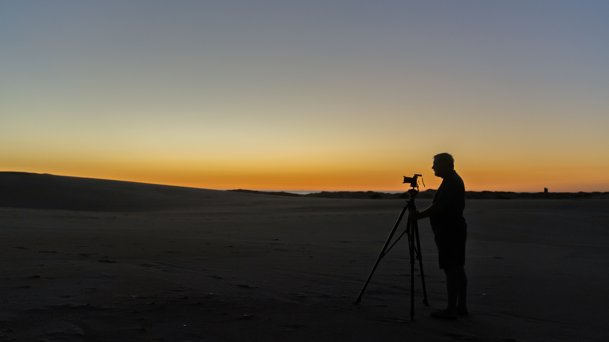Photographer standing on coastal sand dunes at sunrise