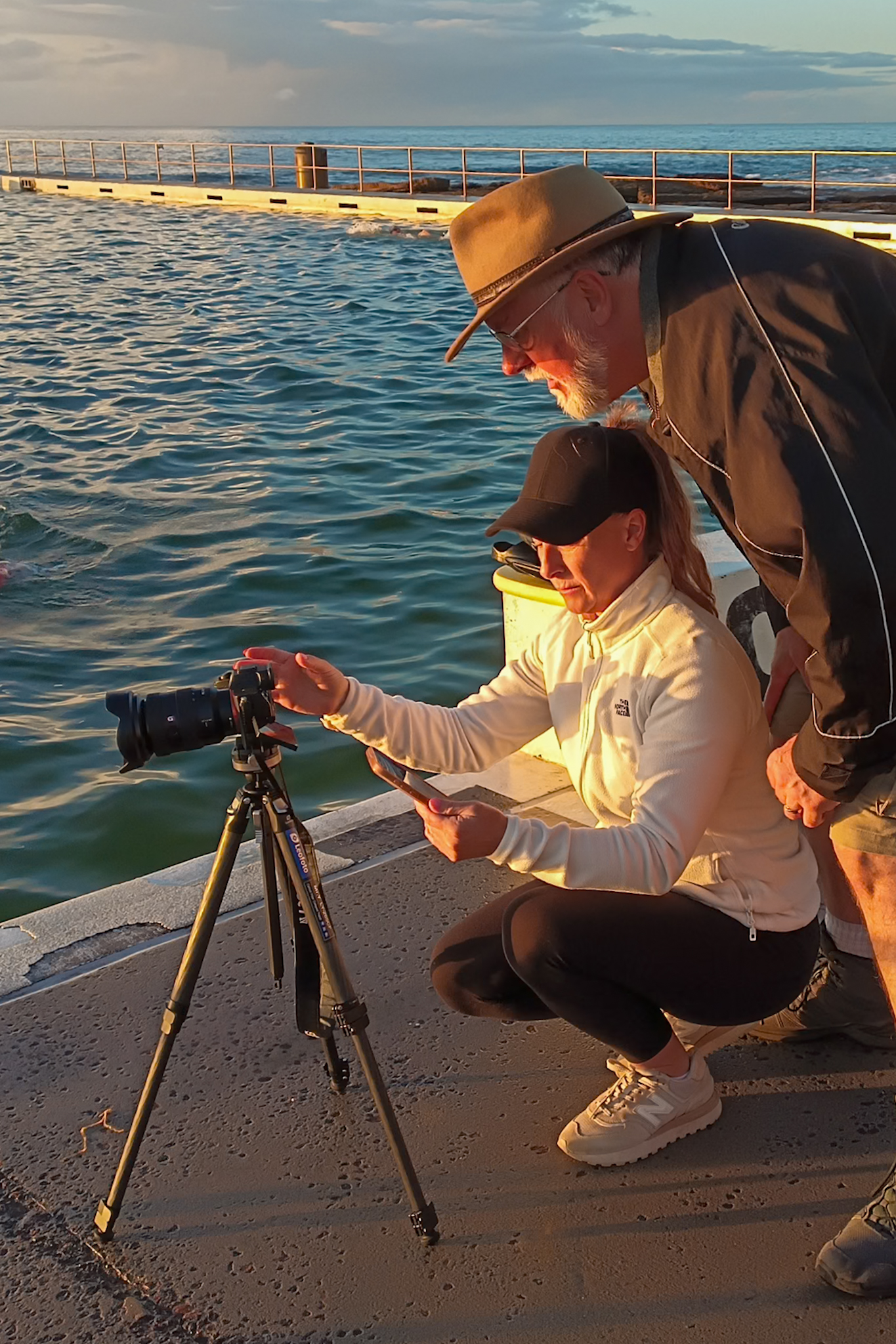 Subscribe to Newsletter - Photography participant receiving camera guidance beside ocean baths during warm coastal light
