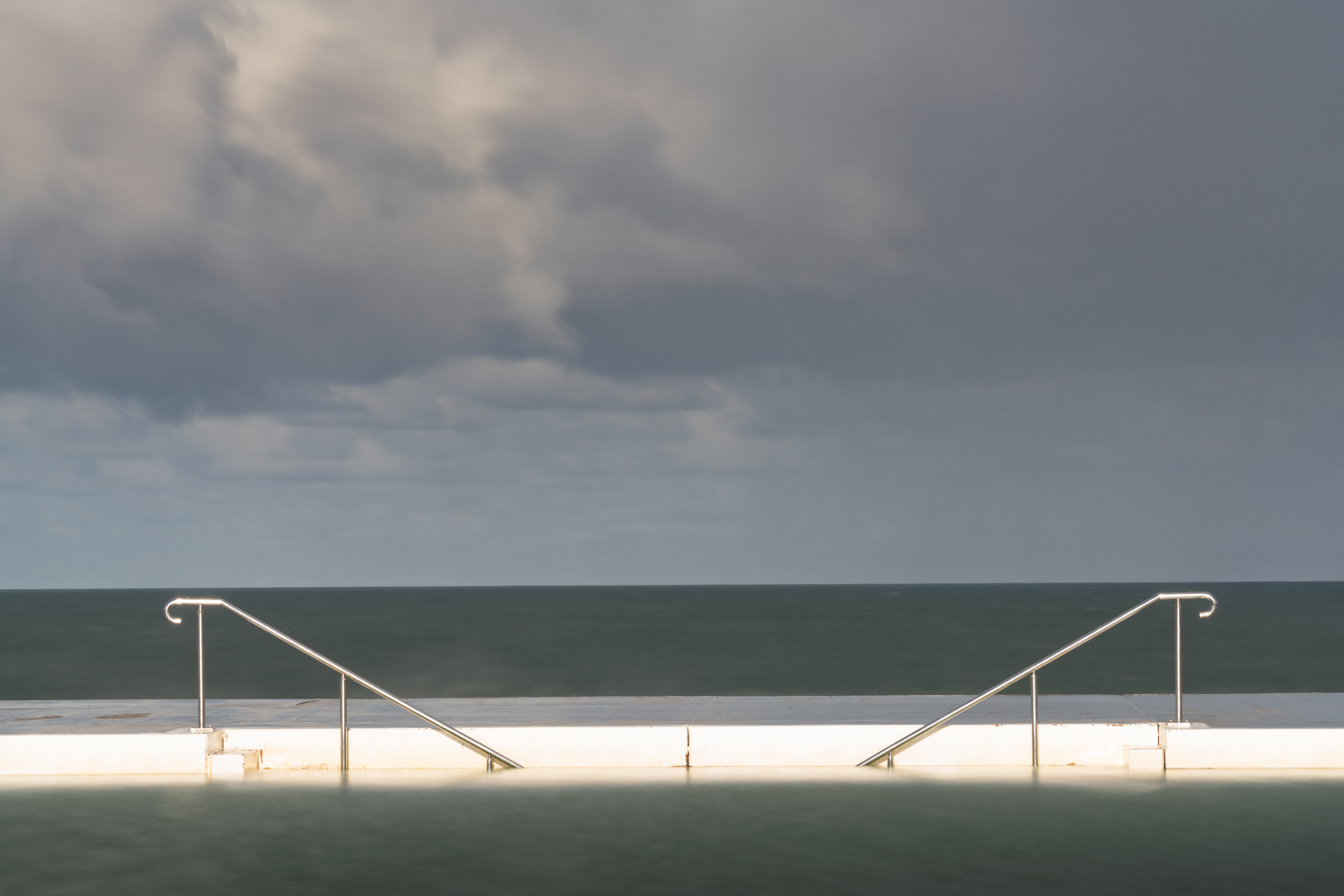 Long exposure black and white photograph of Newcastle Ocean Baths during approaching storm conditions.