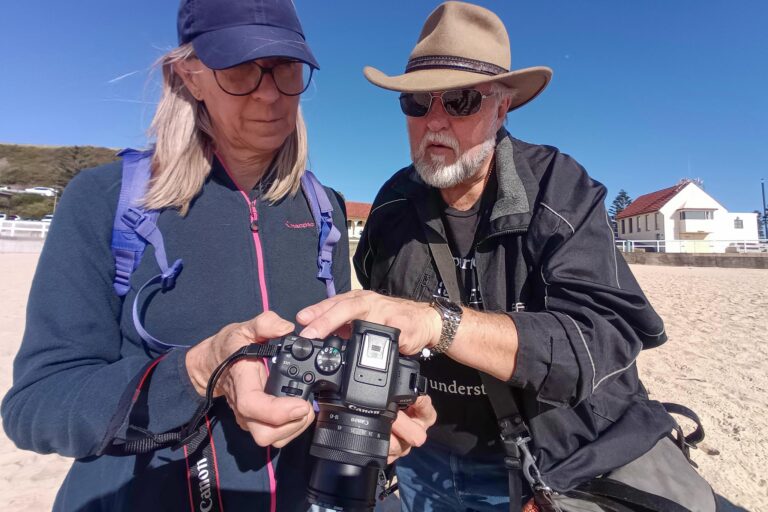 Photography instructor helping a participant with camera settings during a beach workshop