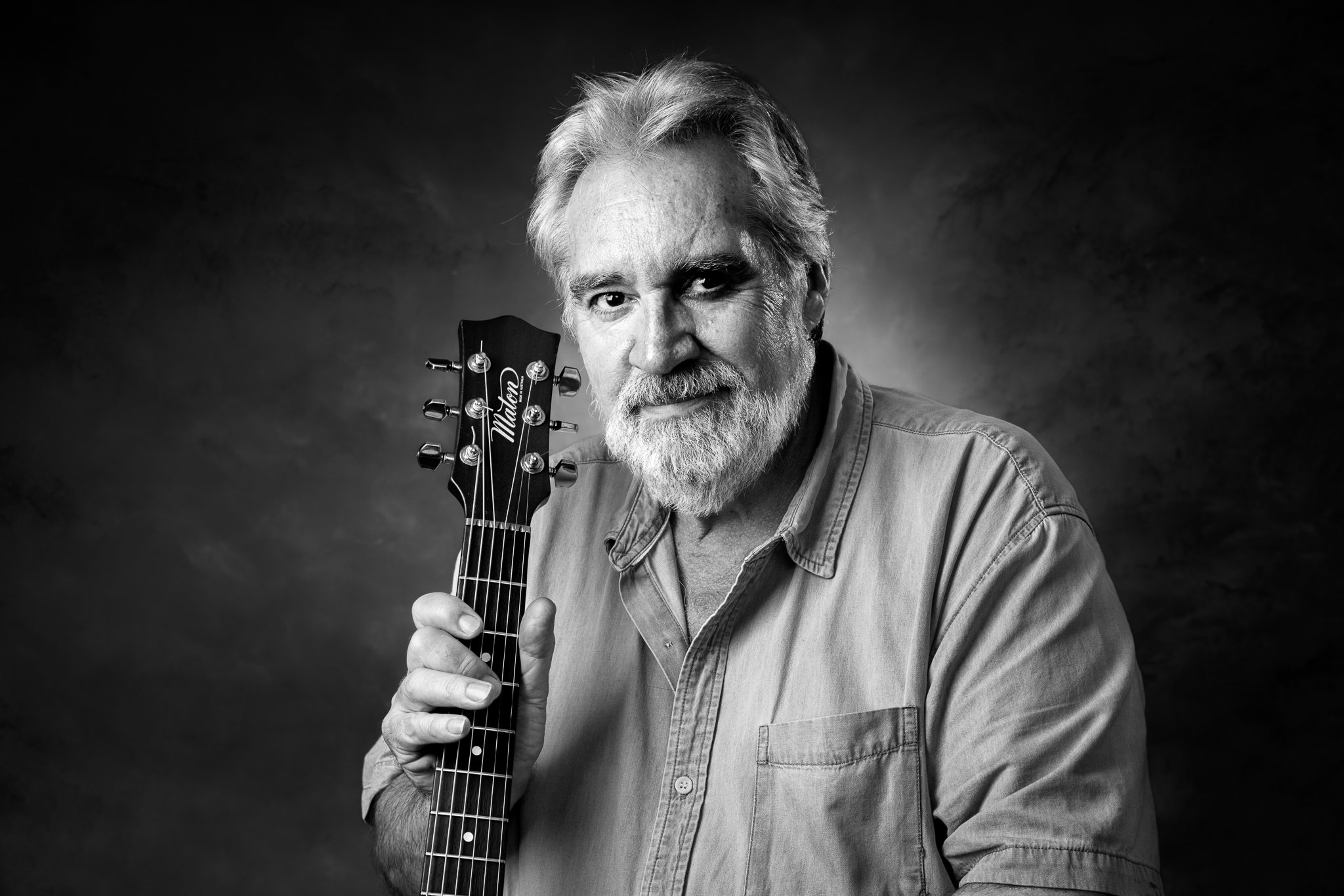 Black and white portrait of a local musician holding an acoustic guitar photographed using studio lighting.