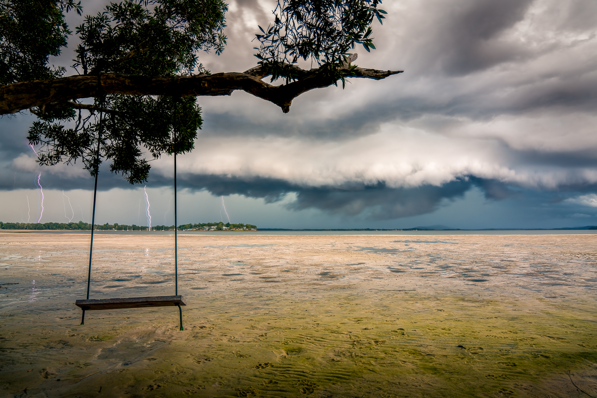 Approaching thunderstorm with lightning over Port Stephens Bay photographed from a swing suspended above the shoreline.